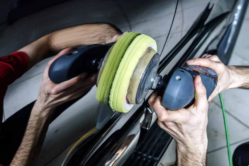 A polisher going over a car's surface with a yellow pad.