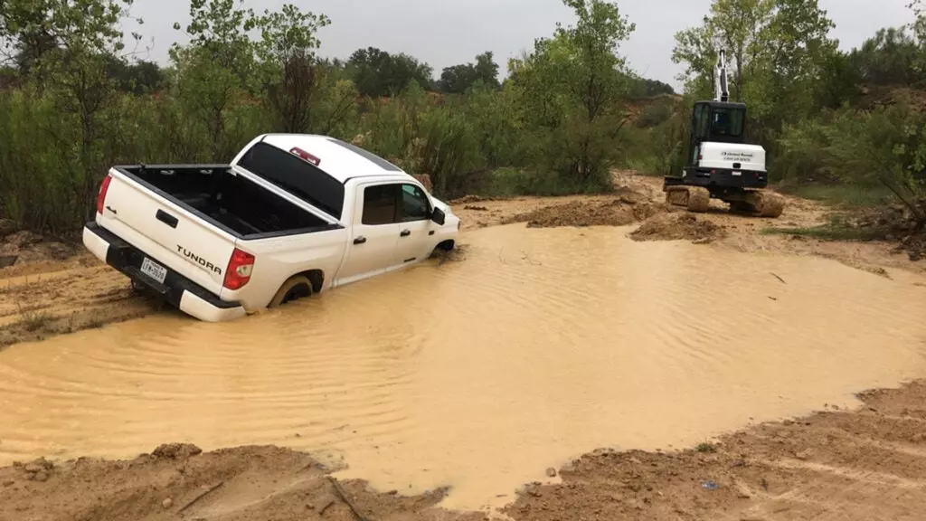 A white Toyota Tundra stuck in a giant mess of mud and a pool of water.
