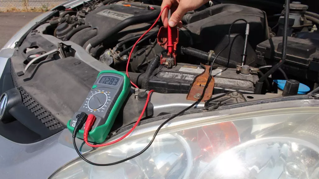 A multimeter is used to check battery voltage on a silver 2003 Acura RSX.
