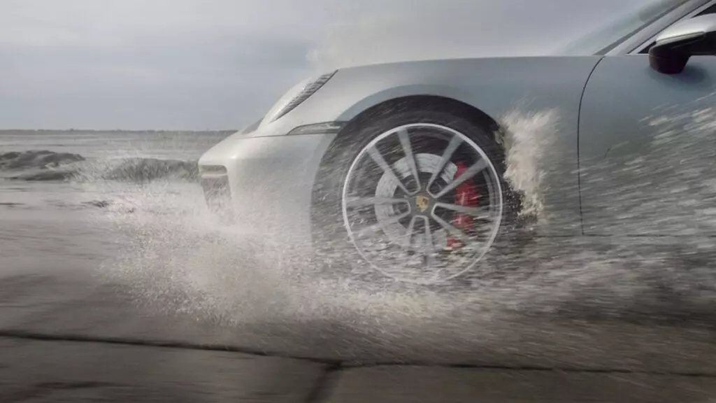 The front-end of a Porsche 911 driving through water.