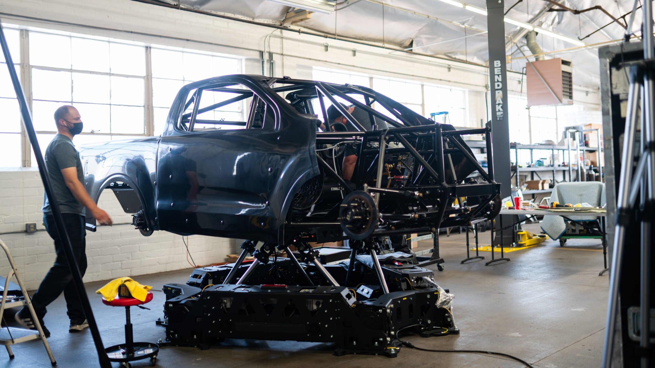 A Pro-4 truck is mounted on six electric motors to simulate movement. In the background is a bright warehouse space with people milling around.