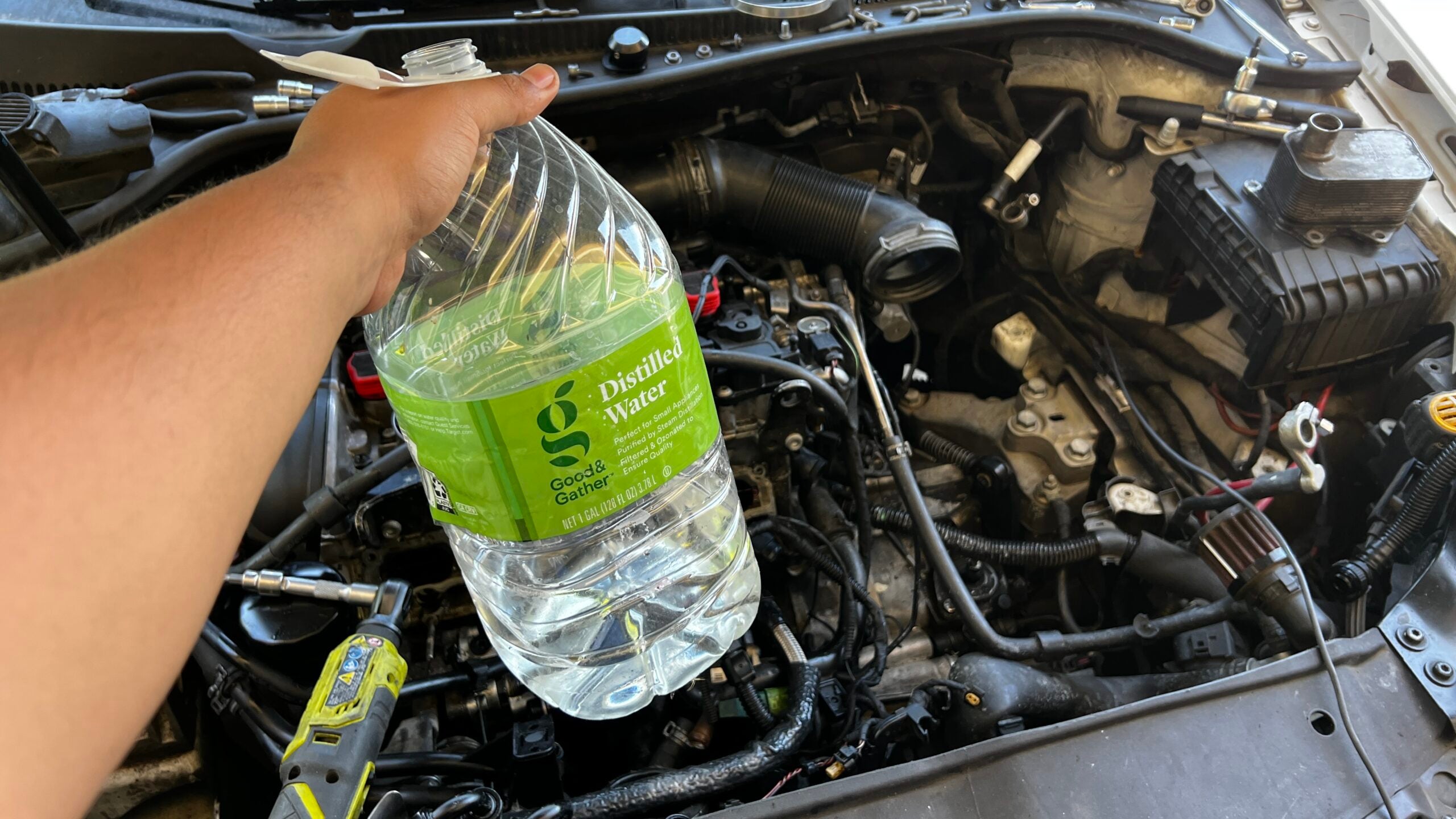 An image of a gallon of distilled water being held above an engine bay. The label on the water gallon is green.