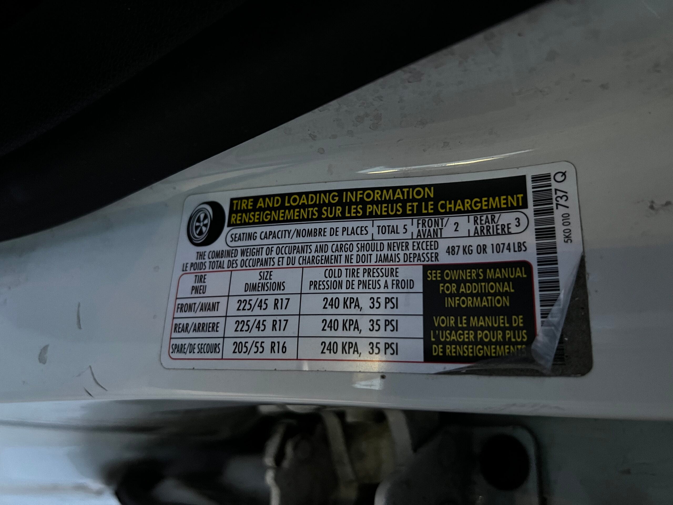 The tire pressure and vehicle weight sticker in the door jamb of a white car. It has a white background, black text, and yellow warning text.