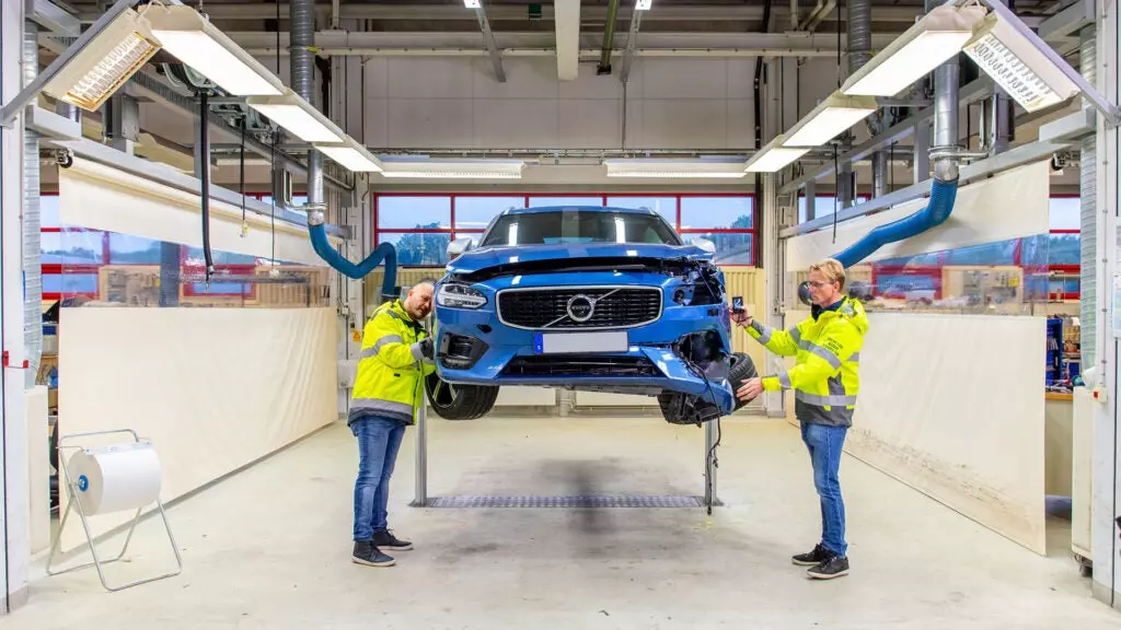 Two Volvo crash researchers inspect a blue wrecked car on a lift.
