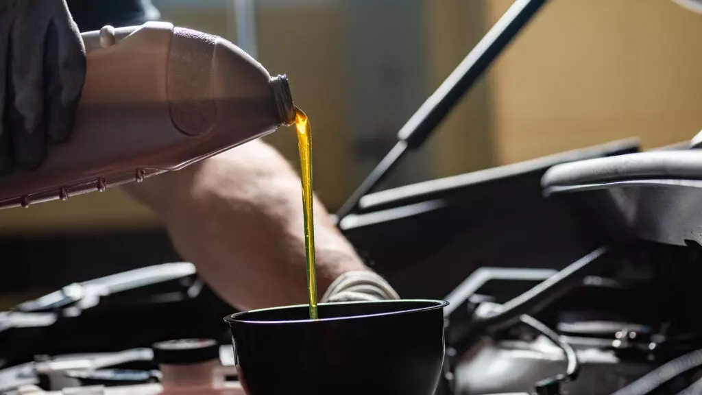 A mechanic pours new oil into the engine through a funnel.