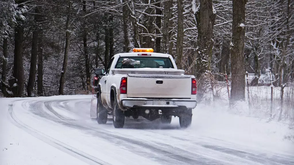 A pickup truck with plow equipment driving on a snowy road.