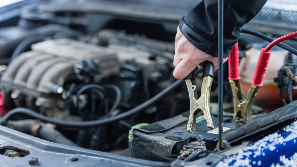 A hand attaching jumper cables to a car battery.