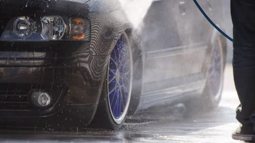 A lowered car with blue wheels rinsed with water.