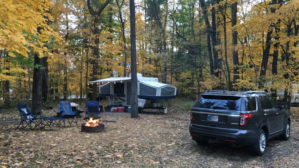 A Ford Explorer at a campsite with a popup camper a fire and camping chairs.