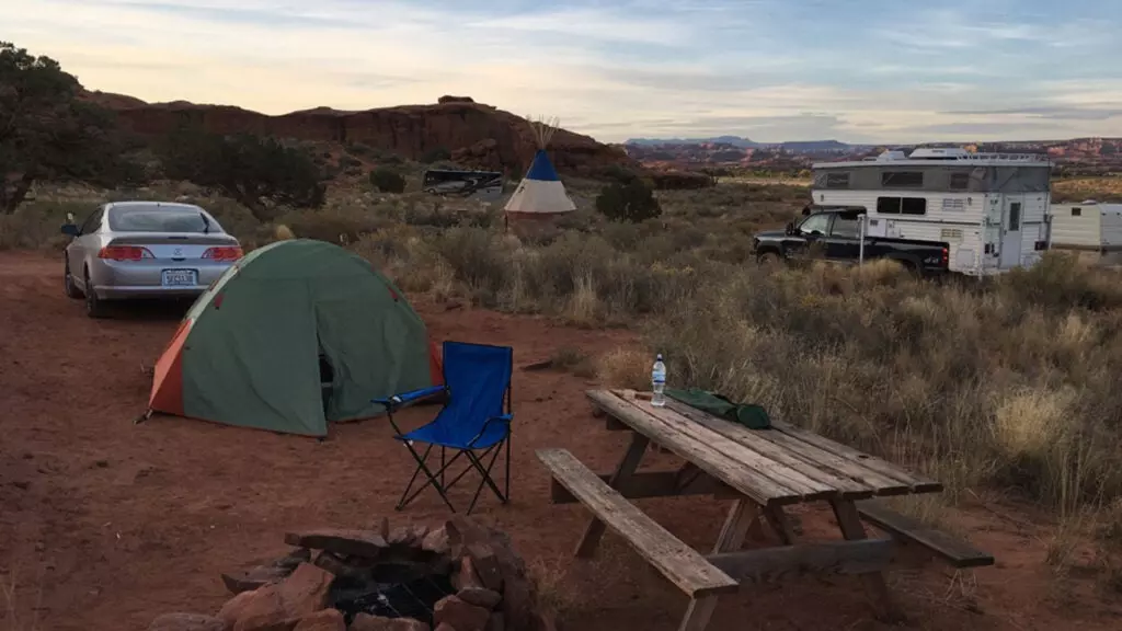 An Acura RSX, a tent, a picnic table, and a fire pit in the foreground of a campsite.